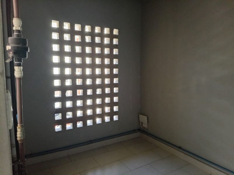 A utility space featuring a decorative breeze block ventilation screen, tiled flooring, and exposed plumbing infrastructure.