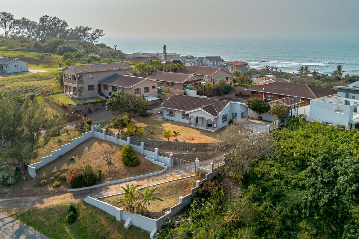 Aerial view of a coastal residential property featuring a tiled roof house, terraced garden, boundary walls, and driveway with ocean views.