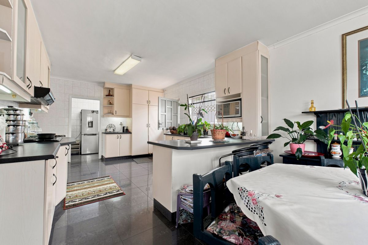 A functional kitchen featuring built-in cabinetry, laminate countertops, a breakfast bar, and tiled flooring, with an adjacent scullery area visible.