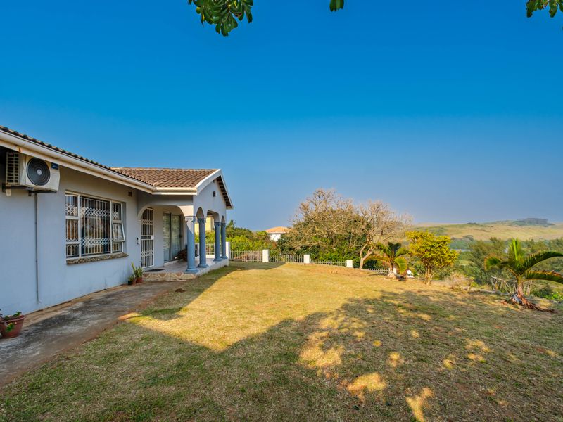 Rear view of the property featuring a covered patio, concrete paving, and a spacious lawn with scenic landscape views.