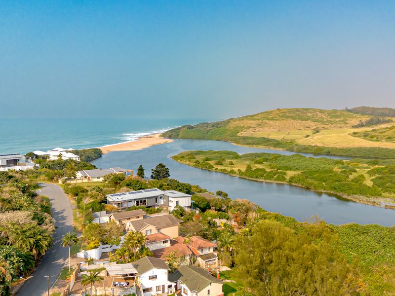 Aerial view of a coastal residential estate featuring homes with solar panels, situated near a river estuary and the ocean.