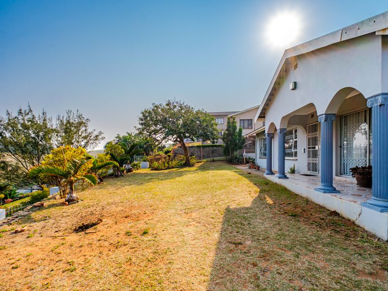 Rear view of the property featuring a covered patio with decorative columns, security gates, and a spacious garden area.