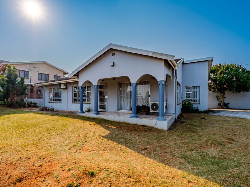 Rear view of the house featuring a covered patio with decorative columns, security gates, and an established garden area.