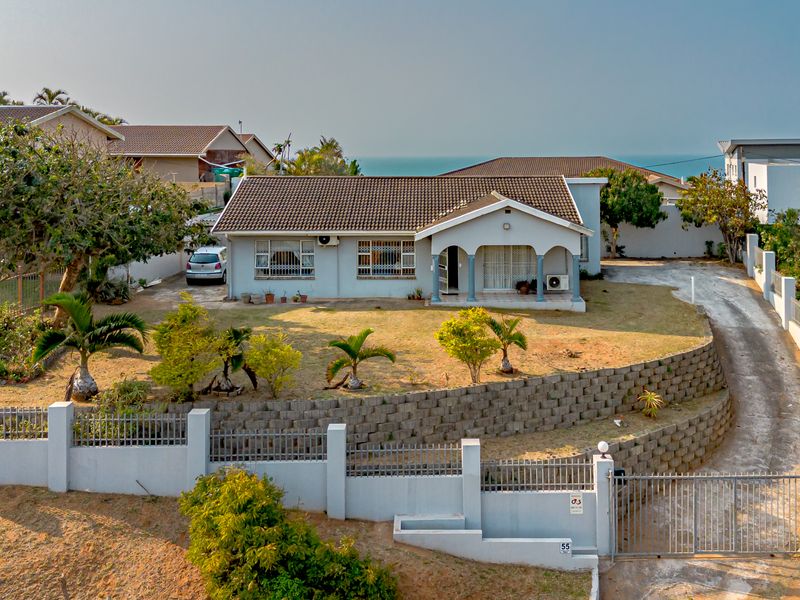 Elevated front view of a single-story residence featuring a tiled roof, covered porch, and a large front garden with a retaining wall and gated driveway.