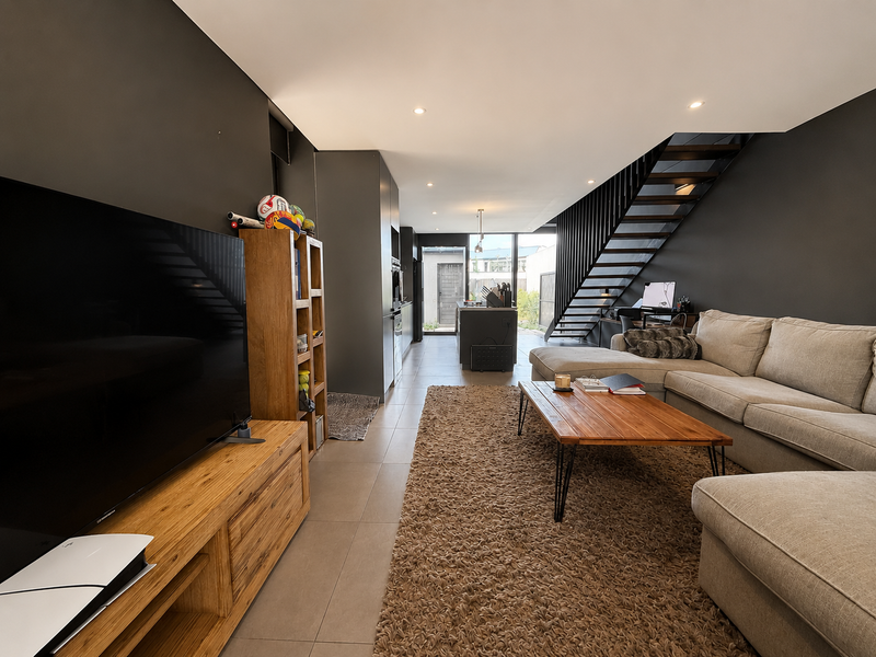 Modern open-plan living area featuring a sleek kitchen, tiled floors, and a striking staircase, creating a seamless flow between cooking and relaxation spaces.
