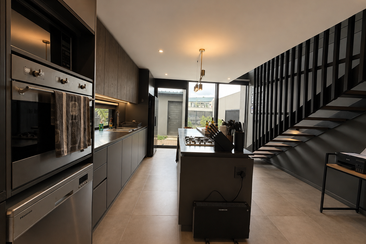 Modern kitchen featuring dark cabinetry, integrated appliances, a central island with gas cooktop, and an adjacent staircase with a sleek metal balustrade.