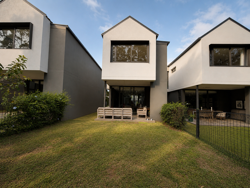 Rear view of a modern two-story residential property featuring a covered patio, landscaped lawn, and secure perimeter fencing.