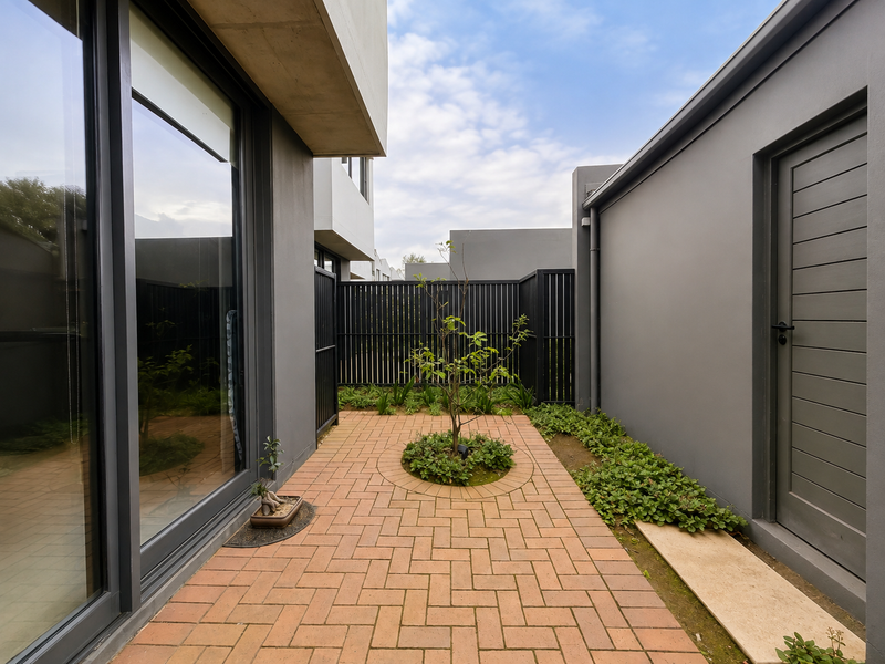 A modern, well-maintained rear courtyard featuring brick paving, landscaped garden beds, and direct access to the home through large sliding glass doors.