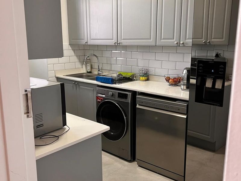 A functional scullery featuring grey shaker-style cabinetry, subway tile backsplash, quartz countertops, and integrated laundry and dishwashing appliances.