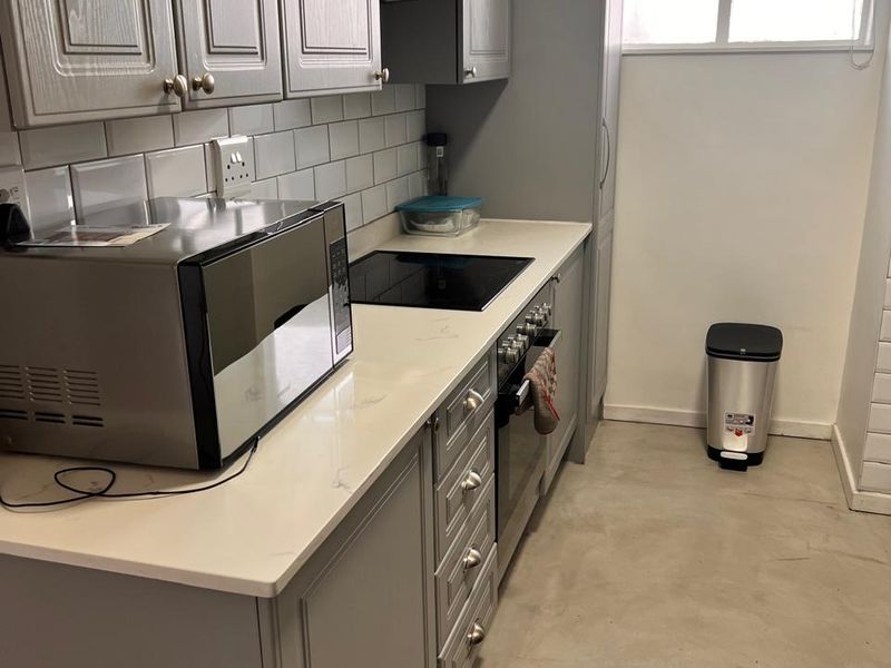 Modern kitchen featuring grey shaker-style cabinetry, stone countertops, subway tile backsplash, and integrated appliances, complemented by polished concrete flooring and natural light.