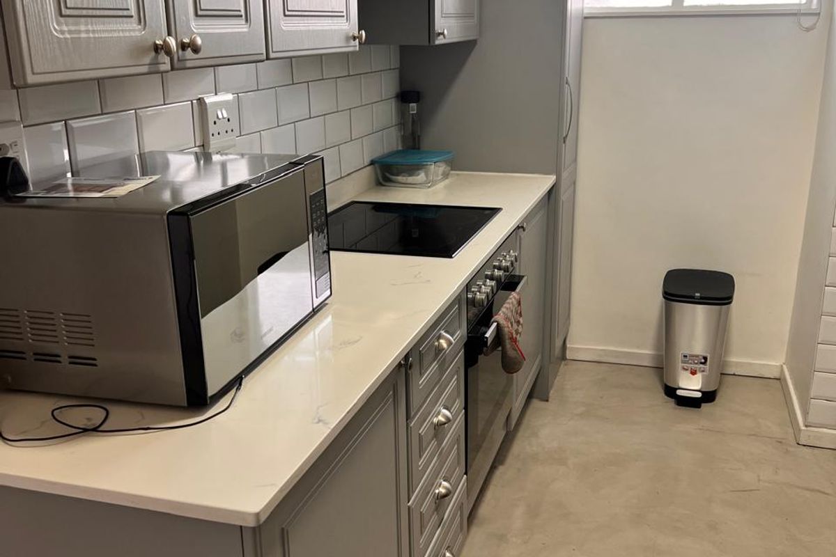 Modern kitchen featuring grey shaker-style cabinetry, stone countertops, subway tile backsplash, and integrated appliances, complemented by polished concrete flooring and natural light.