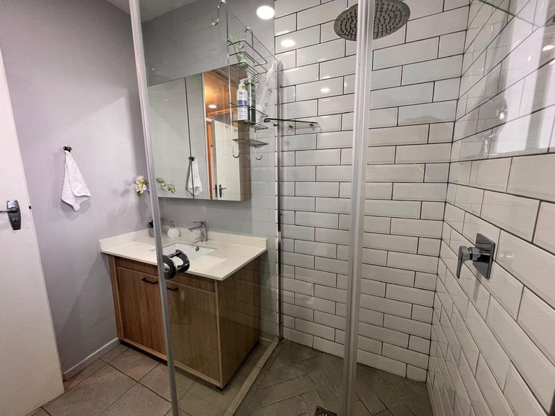 Modern bathroom featuring a wood-finish vanity, white basin, and a spacious walk-in shower with white subway tiling and a rain shower head.