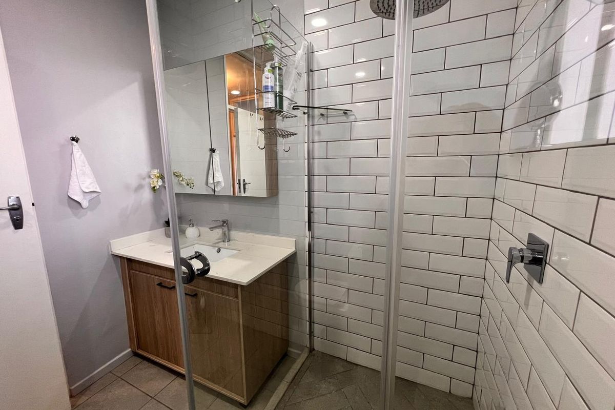 Modern bathroom featuring a wood-finish vanity, white basin, and a spacious walk-in shower with white subway tiling and a rain shower head.