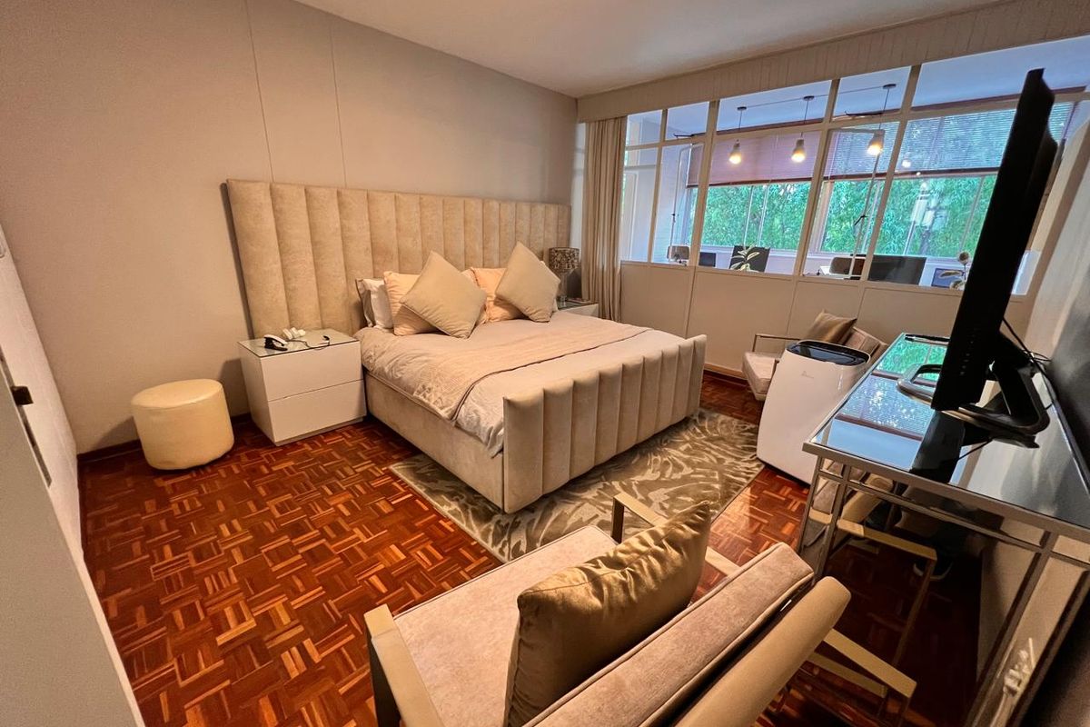 A well-maintained bedroom featuring warm parquet flooring and a unique glass partition wall that allows natural light to flow into the space.