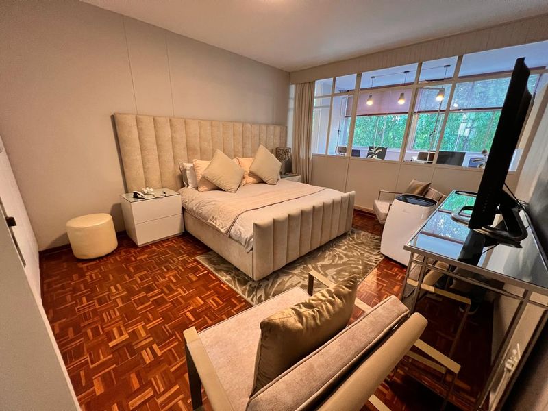 A well-maintained bedroom featuring warm parquet flooring and a unique glass partition wall that allows natural light to flow into the space.