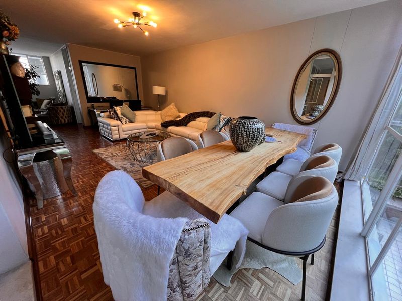 Spacious open-plan living and dining area featuring classic parquet flooring, a modern ceiling light fixture, and large windows providing natural light.