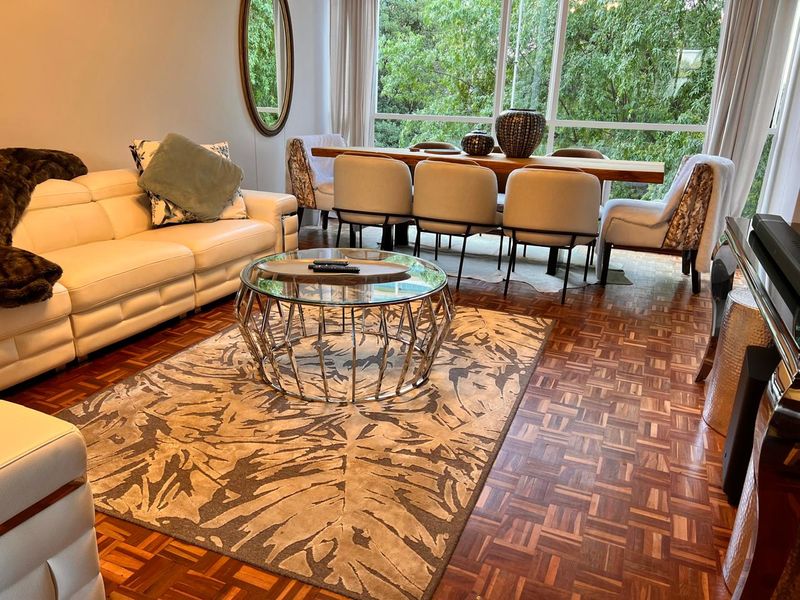 An open-plan living and dining area featuring rich parquet flooring and expansive floor-to-ceiling windows that provide a bright, leafy outlook.