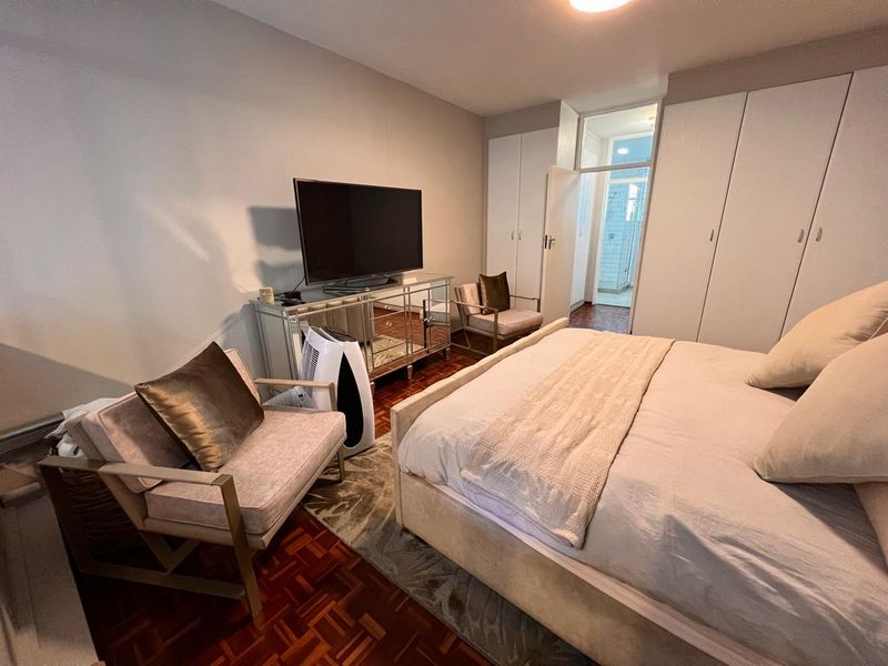 A bedroom featuring classic parquet flooring and ample built-in cupboard storage, with direct access to an adjoining bathroom.