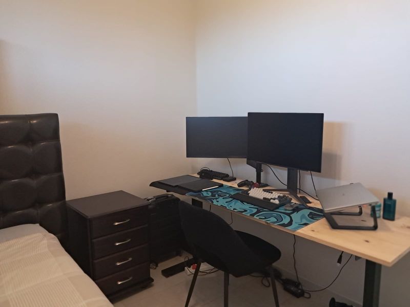 A bedroom space currently utilized as a home office area with neutral wall finishes and tiled flooring.
