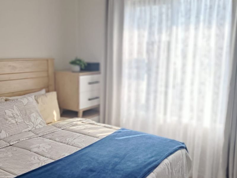 A bright bedroom featuring a ceiling fan and large window with installed curtain rods, providing natural light and a comfortable living space.