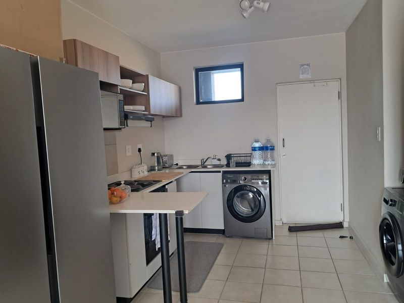 Functional kitchen featuring built-in cabinetry, integrated appliances, tiled flooring, and a dedicated laundry area with washing machine connection.