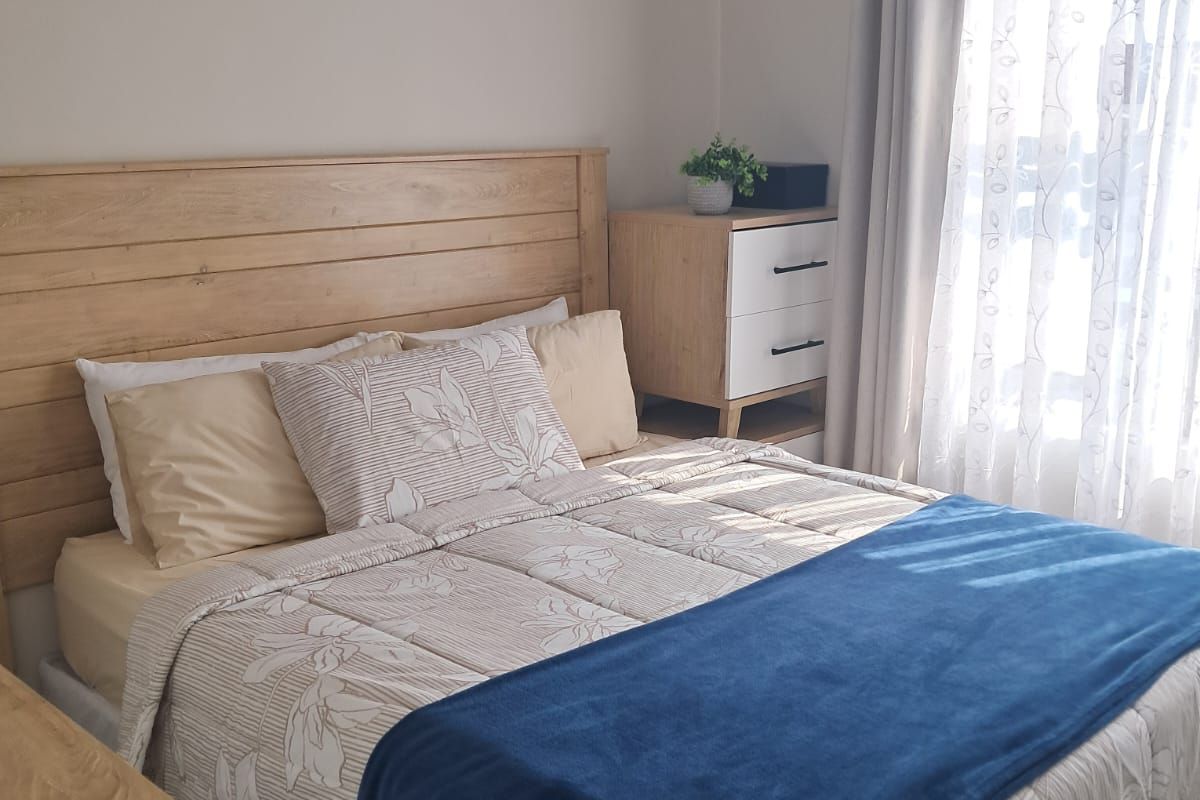 A well-lit bedroom featuring neutral wall tones and a window with installed curtain rod and drapes.