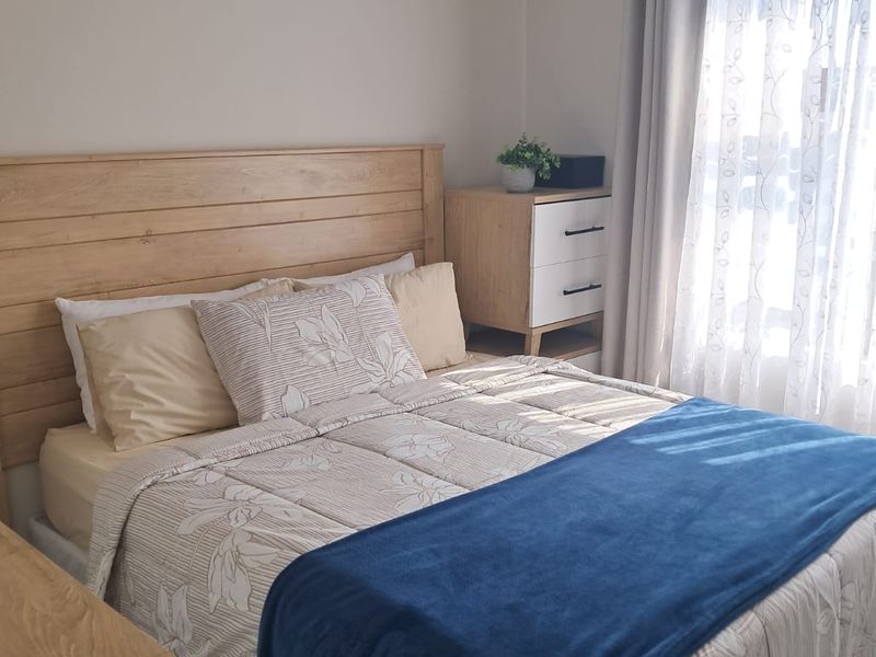 A well-lit bedroom featuring neutral wall tones and a window with installed curtain rod and drapes.