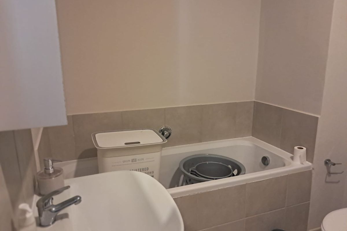 A functional bathroom featuring a bathtub with tiled splashback and a wall-mounted basin.