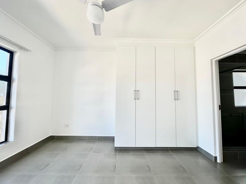 A bright, empty bedroom featuring neutral tiled flooring, built-in cupboards, and a ceiling fan, offering a clean and versatile space.