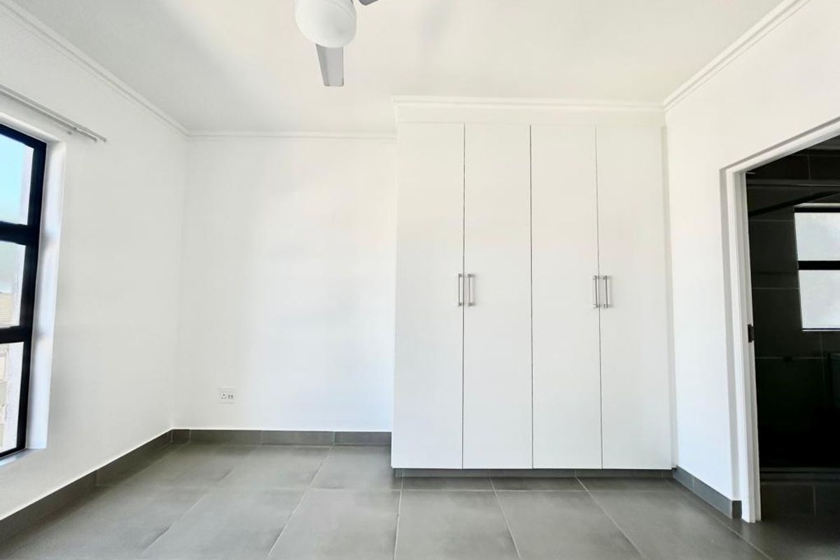 A bright, empty bedroom featuring neutral tiled flooring, built-in cupboards, and a ceiling fan, offering a clean and versatile space.