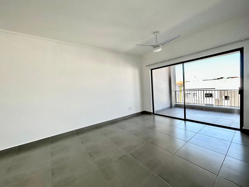 A bright, empty living room featuring large sliding glass doors that open onto a private balcony, complete with tiled floors and a ceiling fan.