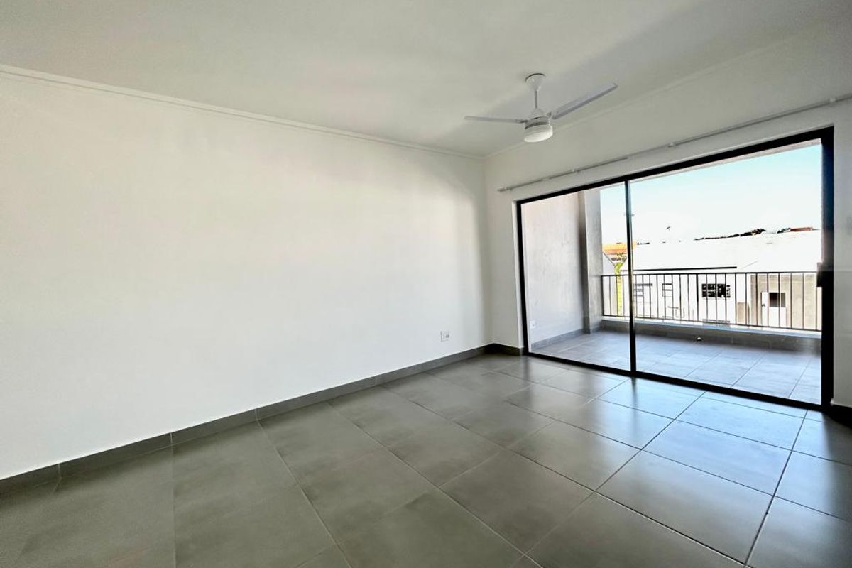 A bright, empty living room featuring large sliding glass doors that open onto a private balcony, complete with tiled floors and a ceiling fan.