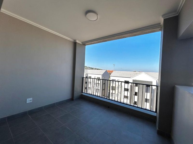 A clean, covered balcony featuring tiled flooring and a metal balustrade, offering an open view of the surrounding apartment complex.