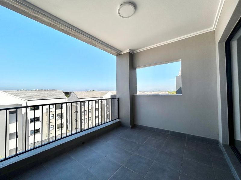 A clean, modern covered balcony featuring tiled flooring, a secure metal balustrade, and an open view of the surrounding apartment complex.