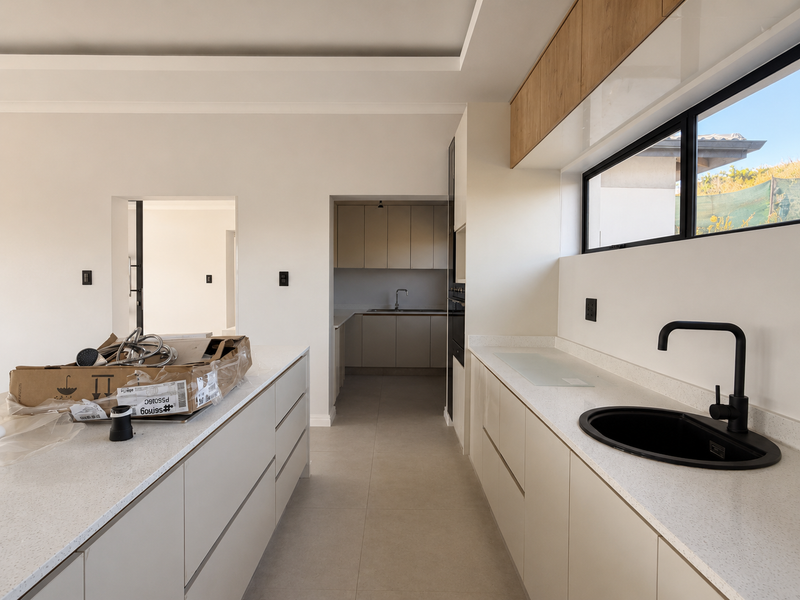 Modern kitchen featuring sleek cabinetry, quartz countertops, a matte black sink fixture, and an adjoining scullery area in a clean, contemporary finish.