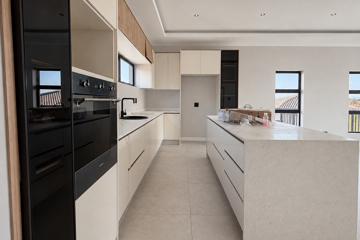 Modern kitchen featuring a large central island, stone countertops, built-in oven, and sleek cabinetry with recessed lighting throughout.