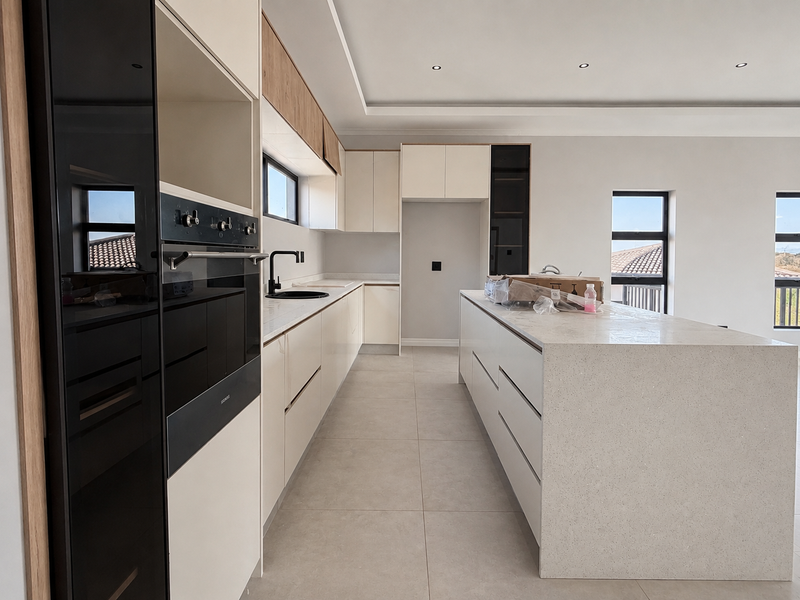 Modern kitchen featuring a large central island, stone countertops, built-in oven, and sleek cabinetry with recessed lighting throughout.