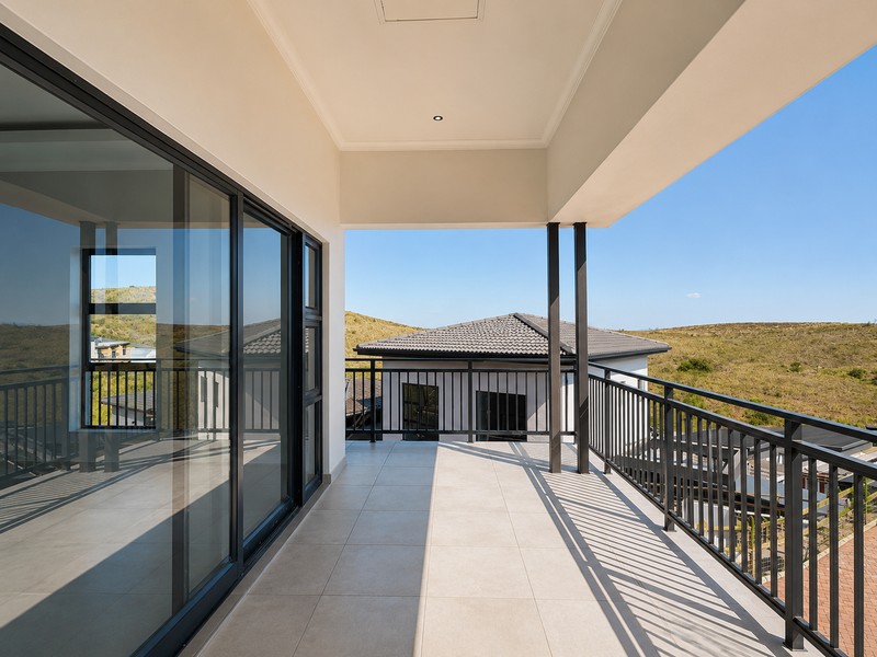 A modern, covered balcony featuring tiled flooring, sleek metal balustrades, and large sliding glass doors with expansive views of the surrounding landscape.