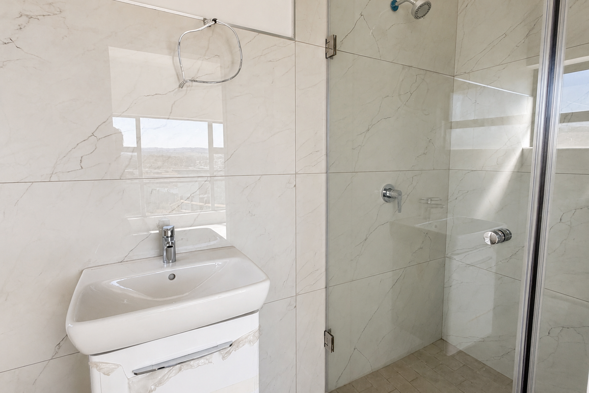 Modern bathroom featuring large format marble-look wall tiles, a vanity basin with mixer tap, and a glass-enclosed shower with a fixed shower head.