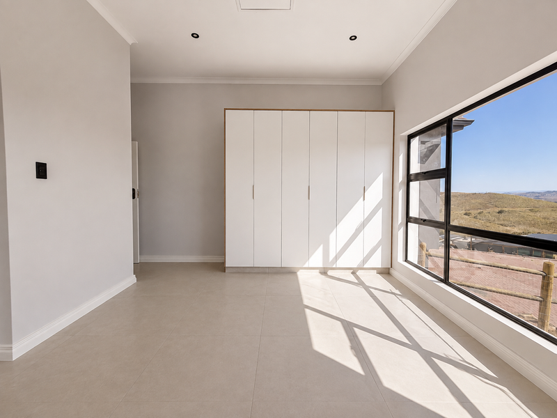 A bright, modern, and empty bedroom featuring neutral tiled floors, built-in cupboards, and a large window offering scenic landscape views.