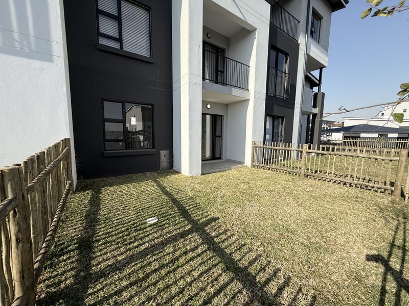 A ground floor apartment unit featuring a private garden area with wooden fencing, a small patio, and modern dark-toned exterior facade finishes.