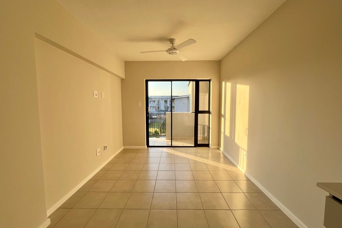 A bright, empty living area featuring neutral tiled flooring, a ceiling fan, and a sliding glass door leading to an outdoor balcony.