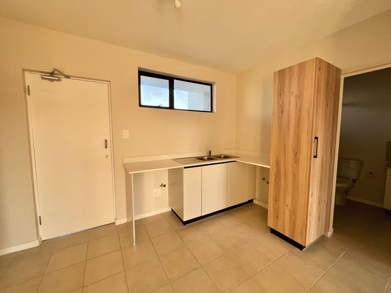 A clean, functional laundry room featuring built-in cabinetry, a stainless steel sink, and tiled flooring, with direct access to an adjacent bathroom.