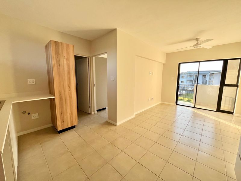 Bright open-plan living area featuring tiled floors, a ceiling fan, and sliding glass doors leading to a private balcony.