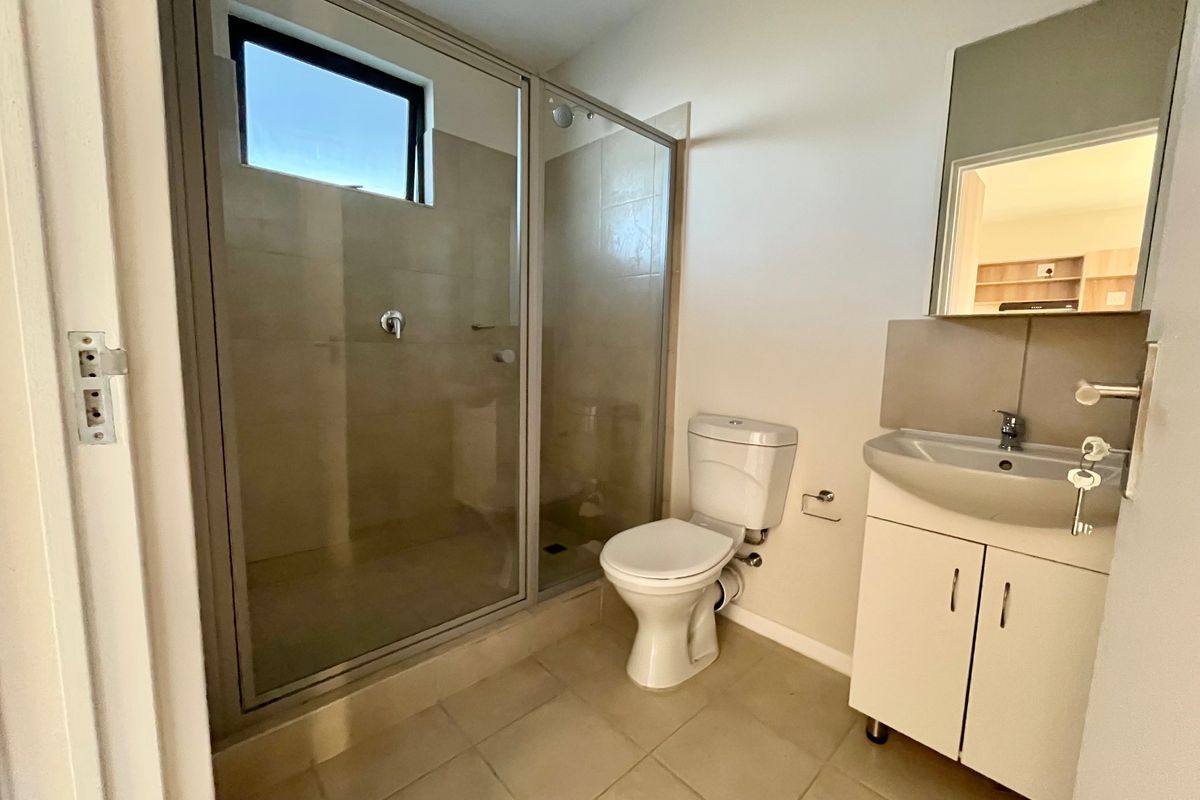 A clean and functional bathroom featuring a glass-enclosed shower, a white toilet, and a vanity unit with a basin and mirror.