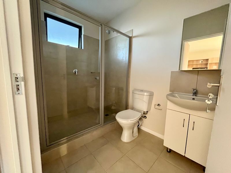 A clean and functional bathroom featuring a glass-enclosed shower, a white toilet, and a vanity unit with a basin and mirror.