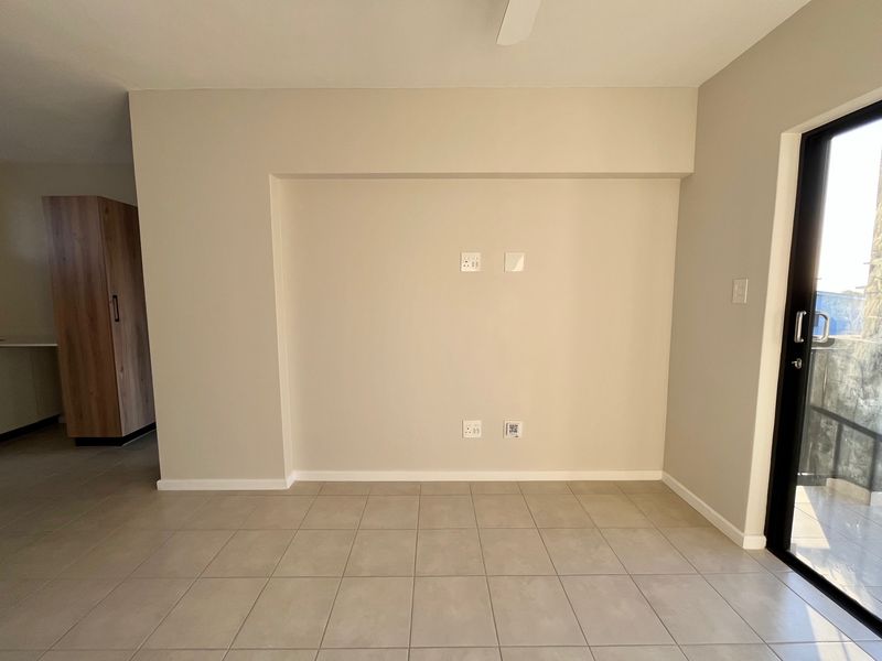An empty, well-maintained living area featuring neutral tiled flooring, modern electrical points, and a sliding glass door providing access to the exterior.