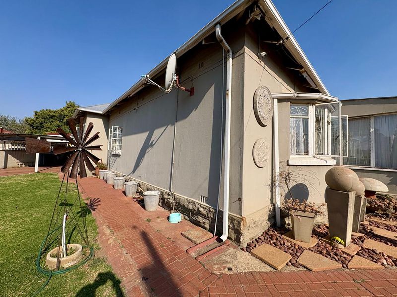 Rear exterior view of the house featuring a brick pathway, bay window, and stone cladding base along the side wall.