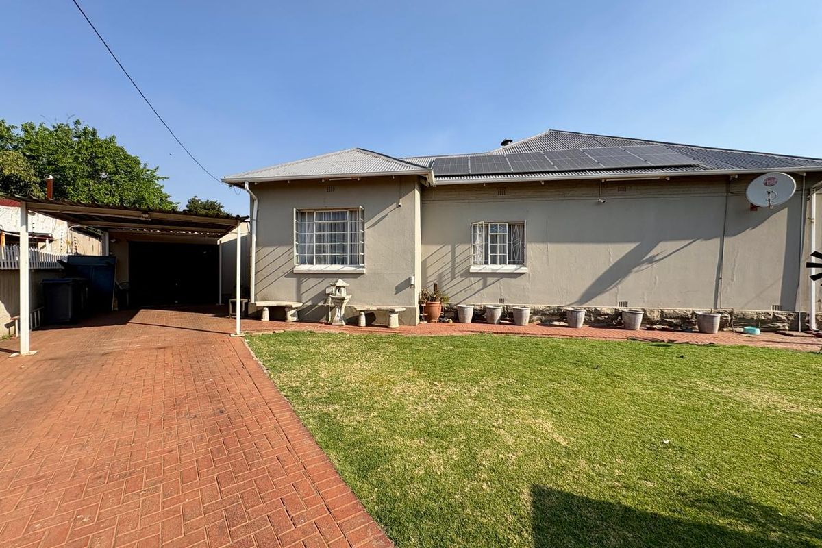 Rear view of the house featuring a brick paved driveway, carport, solar panels on the roof, and a well-maintained lawn.