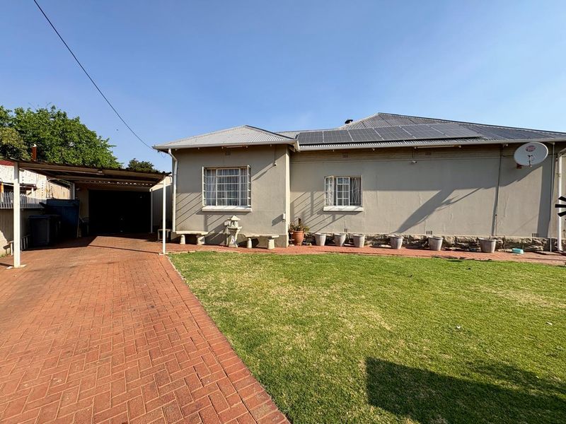 Rear view of the house featuring a brick paved driveway, carport, solar panels on the roof, and a well-maintained lawn.